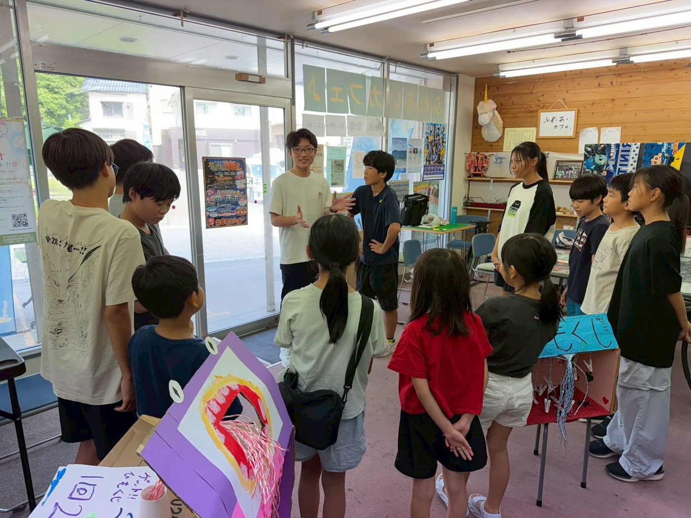 輪になって大人の話を聞く子どもたち。手前に手作りのひもくじの箱が置かれている