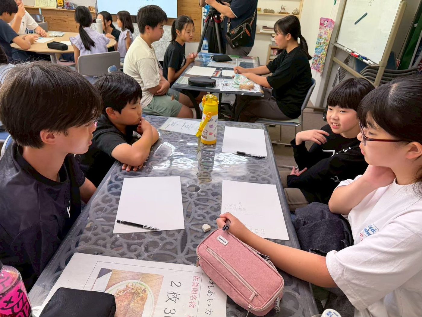 机を囲み、白い紙とペンを前に話し合う子どもたち